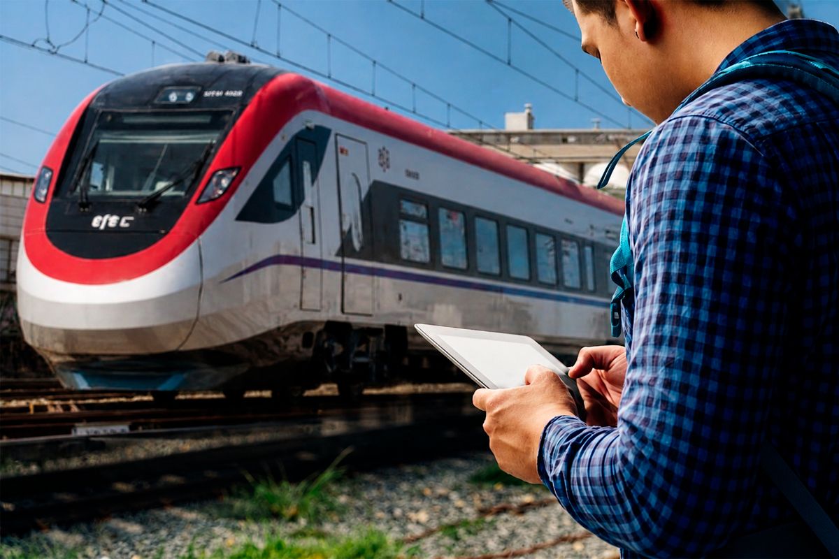 Pasajero revisando información en su tablet junto a la vía, con un moderno tren de EFE de fondo, ilustrando la planificación y tips de viaje.