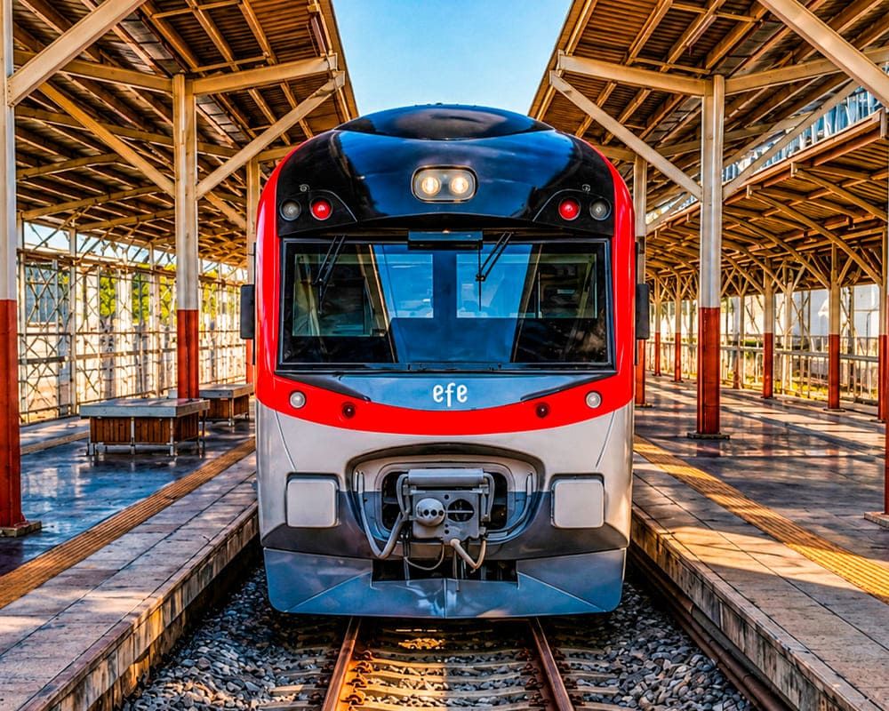Vista frontal del moderno tren UTS de EFE con diseño aerodinámico en rojo y negro, estacionado bajo la estructura clásica de un andén, operando el servicio de larga distancia Santiago-Chillán.