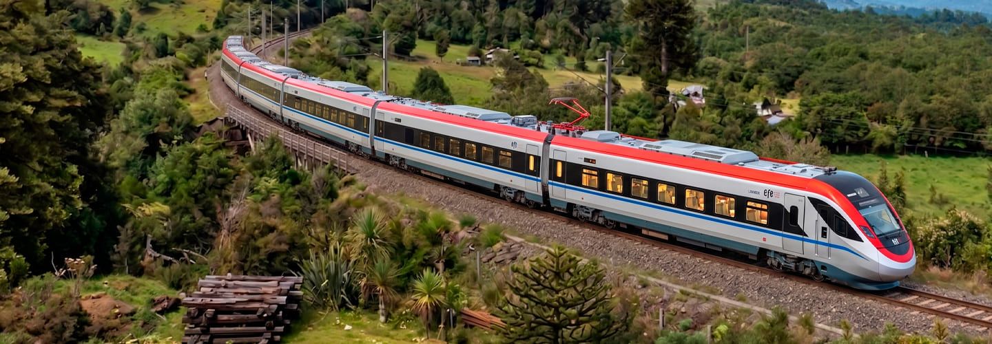 Vista aérea del moderno tren rápido BMU de EFE realizando la ruta Santiago-Curicó, avanzando a través de un paisaje natural rodeado de vegetación.